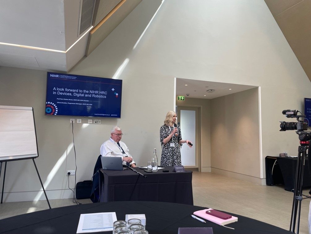 Photo of Olivia Brookes, Programme Manager, holding a microphone and speaking at the HRC DDR launch event alongside a colleague sitting next to her at a table